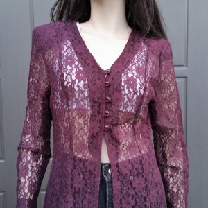 Puede incluir: Una larga chaqueta de encaje color burdeos con cierre de botones. La chaqueta es transparente y tiene un patr&oacute;n floral.