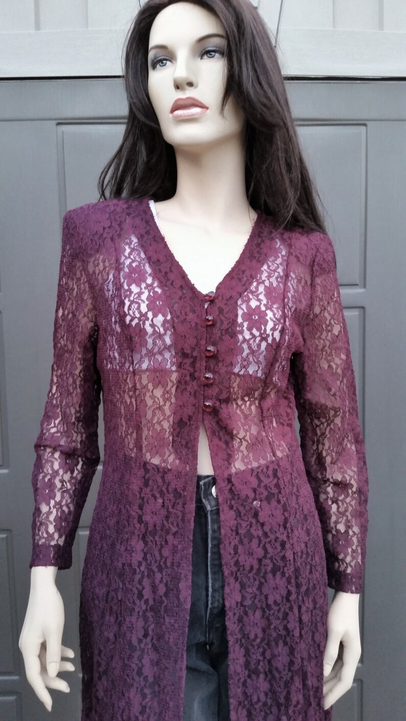 Puede incluir: Una larga chaqueta de encaje color burdeos con cierre de botones. La chaqueta es transparente y tiene un patr&oacute;n floral.