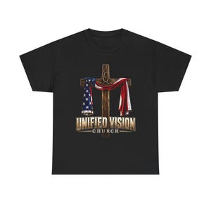 May include: A black t-shirt featuring a graphic of a wooden cross draped with an American flag. A rope is tied around the top of the cross. Below the cross, the text reads UNIFIED VISION CHURCH in a distressed, metallic-toned, block-style font.