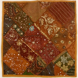 May include: A square throw pillow with a patchwork design featuring various shades of brown, gold, and green. The pillow is adorned with sequins, beads, and embroidery, creating a textured and intricate pattern.