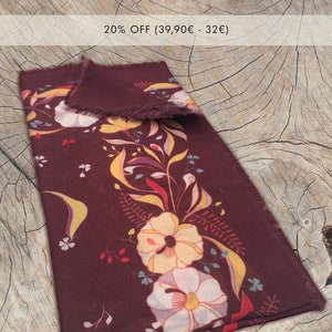 以下が含まれることがあります： 黄、白、赤の色合いの花柄が施された、ワインレッドのシルクスカーフ。スカーフはフリンジの縁取りがあり、半分に折り畳まれています。画像の上部に「20% OFF (39,90€ - 32€) 」というテキストが表示されています。