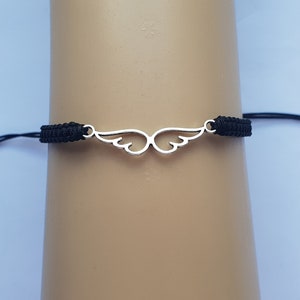 May include: A black cord bracelet with a silver wing charm. The bracelet is adjustable with a sliding knot.