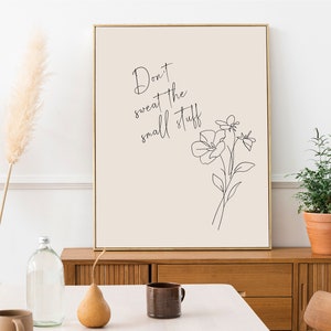 Może przedstawiać: Beżowy wydruk w ramie z czarnym rysunkiem liniowym kwiatu i tekstem "Don't sweat the small stuff". Wydruk wisi na białej ścianie nad drewnianym komodą.
