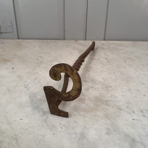May include: A rusty metal fireplace poker with a twisted handle and a decorative, stylized letter 'C' at the end.