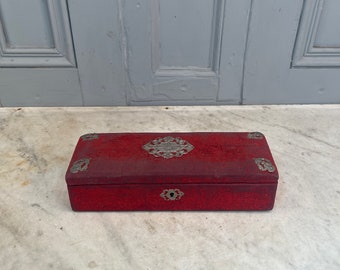 Puede incluir: Una caja de madera roja con detalles en metal plateado y una cerradura. La caja tiene una superficie texturizada y está decorada con diseños de metal plateado ornamentados.