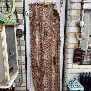 May include: A brown fabric with a white geometric pattern hangs on a white door. The fabric has a rough texture and is slightly faded.