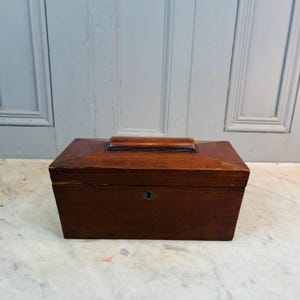 May include: A wooden box with a hinged lid and a keyhole. The box is dark brown and has a simple design.