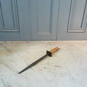 Puede incluir: Un afilador de cuchillos de acero vintage con un mango de asta de ciervo marr&oacute;n y blanco. El afilador tiene una virola de lat&oacute;n y est&aacute; sobre una superficie de m&aacute;rmol blanco.
