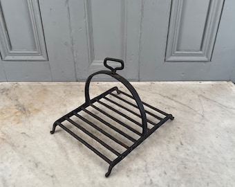 May include: A black metal fireplace grate with a handle. The grate is designed to hold logs over a fire.