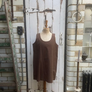 Puede incluir: Un vestido marrón sin mangas en un maniquí, expuesto contra una puerta de madera blanca con un fondo rústico.