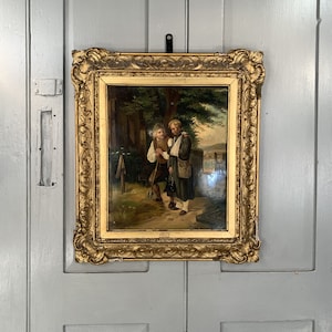 May include: A framed oil painting depicting two men in a rural setting. The men are dressed in 19th-century clothing and are standing near a tree and a stone marker. The painting has a gold frame.