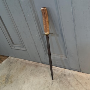 Puede incluir: Un pincho largo, delgado y met&aacute;lico con un mango de asta de ciervo marr&oacute;n. El pincho est&aacute; oxidado y tiene un anillo de lat&oacute;n en la parte superior del mango.