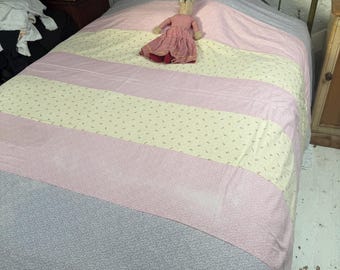 May include: A bed with a striped quilt in shades of pink, yellow, and gray. A vintage doll in a red and white striped dress rests on the quilt. The bed frame is made of metal.