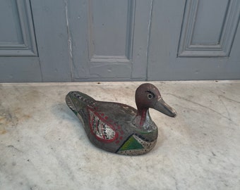 May include: A hand-painted wooden duck decoy with green, red, and white paint. The duck has a brown head and a long, thin beak.