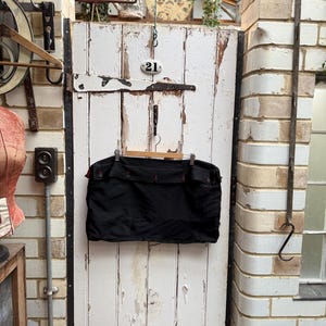 May include: A black garment bag with red accents hanging on a white wooden door with a black metal handle and the number "21" on a white plaque. The door is weathered and has peeling paint.