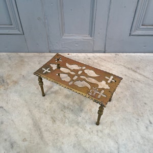 Può includere: Un sottopentola in ottone con un design decorativo a taglio. Il sottopentola ha quattro gambe ed è fatto di metallo massiccio.