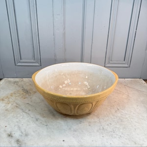 Può includere: Una ciotola in ceramica gialla con interno bianco. La ciotola ha un motivo decorativo all'esterno ed è appoggiata su una superficie di marmo. È un articolo per la cucina.