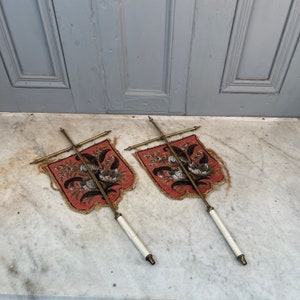 May include: Two antique embroidered wall hangings with floral designs on a red background. The hangings are mounted on brass rods with white handles.