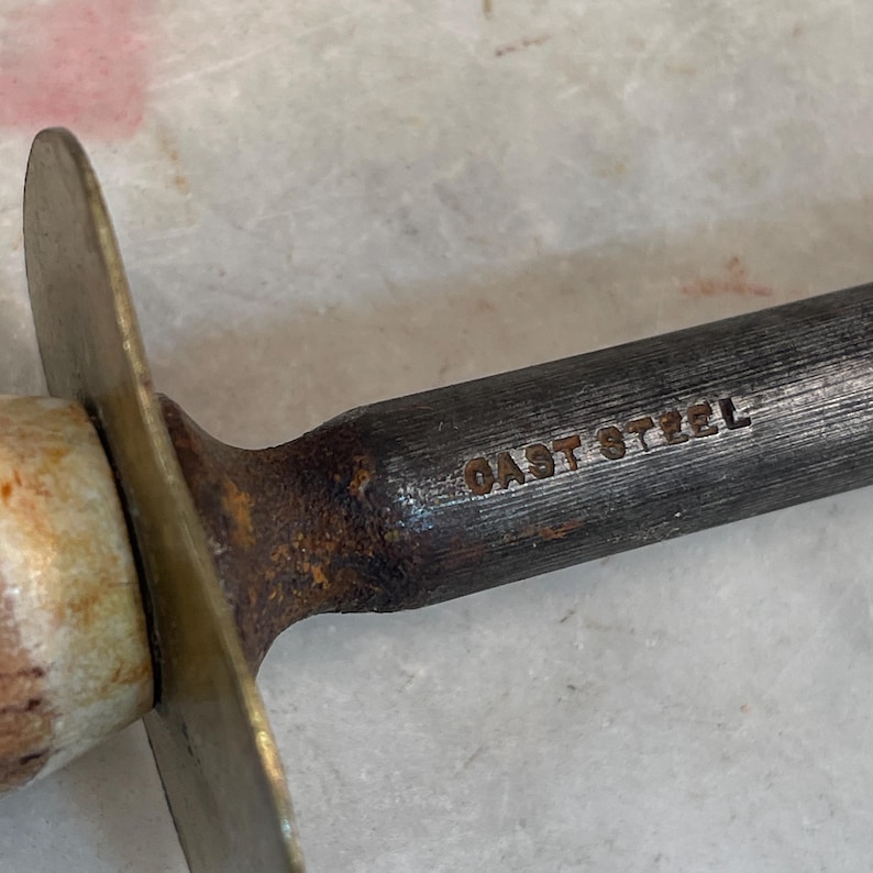 Puede incluir: Primer plano de un afilador de cuchillos de metal con mango de lat&oacute;n y las palabras "CAST STEEL" grabadas en el metal.