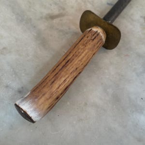 Puede incluir: Un afilador de cuchillos de acero vintage con mango de madera. El mango es de madera marr&oacute;n claro con una punta blanca. La parte met&aacute;lica del afilador es plateada y tiene una tapa de lat&oacute;n.