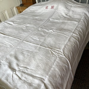 May include: A white linen bed sheet with red embroidered lettering that says "Je t'aime" on a white metal bed frame.