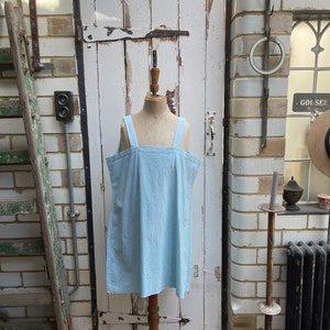 Könnte beinhalten: Ein hellblaues, ärmelloses Kleid auf einem weißen Mannequin vor einem Hintergrund aus Backstein.