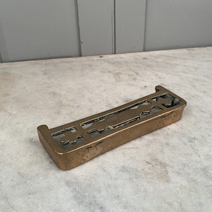 Puede incluir: Un enrejado de chimenea de latón con un diseño decorativo. El enrejado está hecho de latón macizo y tiene una forma rectangular.