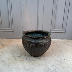 May include: A dark brown metal planter with a scalloped rim and a decorative pattern of curved lines. The planter has a green patina.