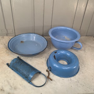 Pode incluir: Quatro itens de cozinha de esmalte azul: uma tigela pequena, uma tigela maior com alça, uma forma redonda para bolo e um ralador.