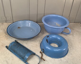 May include: Four blue enamelware kitchen items: a small bowl, a larger bowl with a handle, a round cake pan, and a grater.