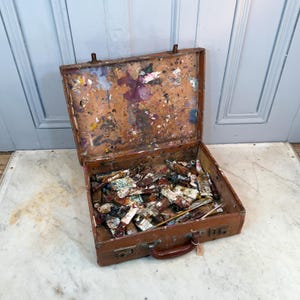 May include: A well-used, open brown leather artist's case, stained with dried paint in multiple colours. The case contains numerous used paint tubes and a few brushes, indicating a well-loved set of art supplies.
