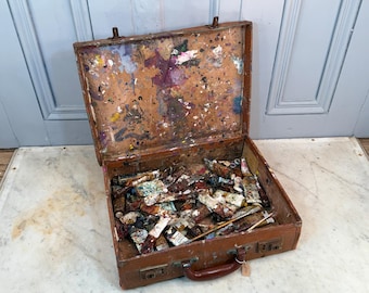 May include: An open, vintage brown leather artist's case, splattered with dried paint in various colors. The case is filled with used paint tubes and a few paint brushes, suggesting a well-loved set of art supplies.
