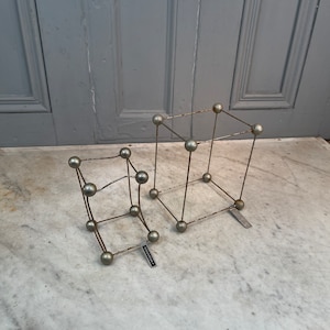 May include: Two silver metal wire sculptures in the shape of cubes. The smaller cube is bent at a 90-degree angle.