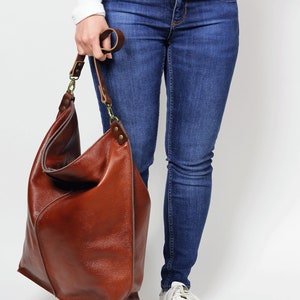 Peut inclure: Un grand sac fourre-tout en cuir marron avec une longue bandouli&egrave;re. Le sac est ample et d&eacute;contract&eacute;, avec un design simple.