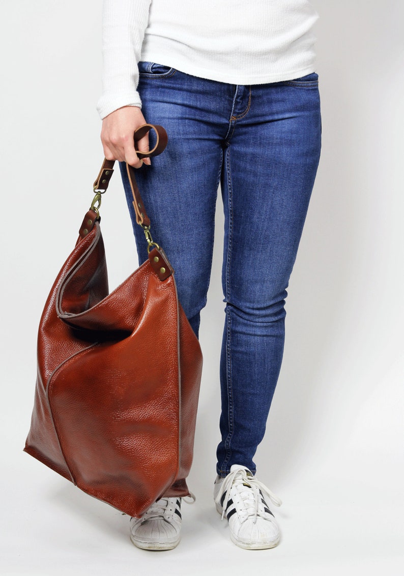 Peut inclure: Un grand sac fourre-tout en cuir marron avec une longue bandouli&egrave;re. Le sac est ample et d&eacute;contract&eacute;, avec un design simple.