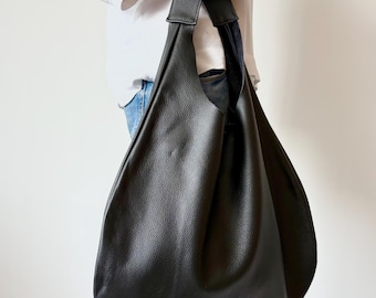 Puede incluir: Un bolso hobo grande de color negro con superficie texturizada y una correa de hombro ancha integrada. El bolso presenta una silueta holgada y sin estructura que se estrecha hacia la parte superior, creando una forma de gota de agua.