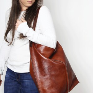Peut inclure: Une femme portant une chemise blanche &agrave; manches longues et un jean bleu porte un grand sac fourre-tout en cuir marron.