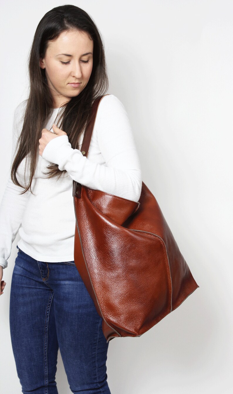 Peut inclure: Une femme portant une chemise blanche &agrave; manches longues et un jean bleu porte un grand sac fourre-tout en cuir marron.