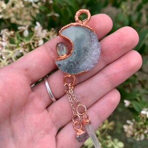 May include: A copper crescent moon pendant with a green and white agate stone, a labradorite stone, and a clear quartz crystal hanging from it.