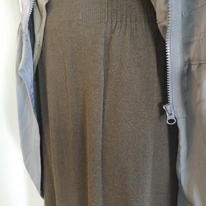 May include: A dark olive green knit skirt with a ribbed waistband is partially covered by a light green jacket. The jacket has a zipper closure and a light blue lining. The skirt is a solid color and has a vertical ribbed texture.