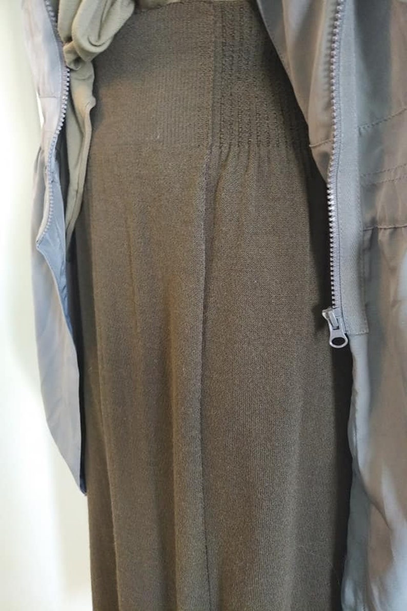 May include: A dark olive green knit skirt with a ribbed waistband is partially covered by a light green jacket. The jacket has a zipper closure and a light blue lining. The skirt is a solid color and has a vertical ribbed texture.