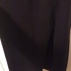 May include: Close-up of a black garment, possibly a skirt or dress, with a side slit. The fabric appears to be a soft, knit material. The hemline is slightly curved. The garment is hanging against a white door frame.