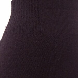 May include: Close-up of a black garment, possibly leggings or tights, with a ribbed waistband. The fabric appears to be a soft, knit material. The image focuses on the waist area, showing the texture and construction.