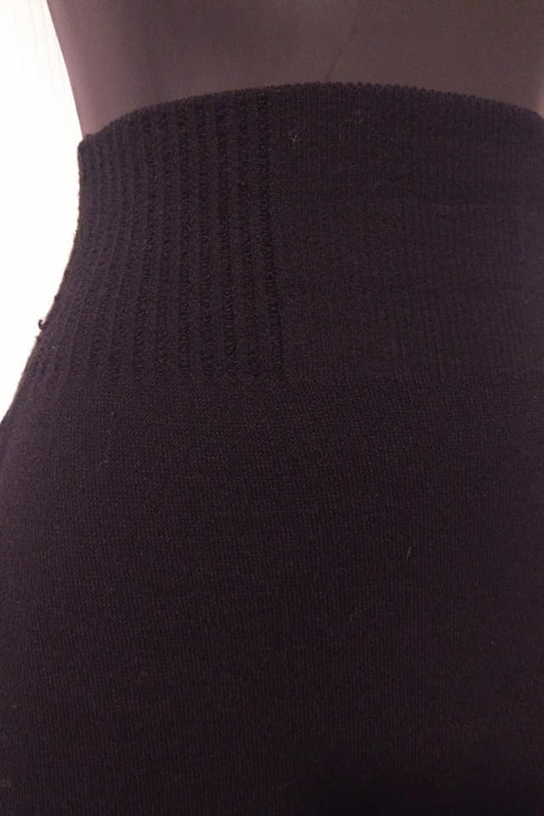 May include: Close-up of a black garment, possibly leggings or tights, with a ribbed waistband. The fabric appears to be a soft, knit material. The image focuses on the waist area, showing the texture and construction.