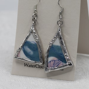 Può includere: Un paio di orecchini triangolari argentati con motivi floreali blu e rosa all'interno. Gli orecchini sono su una carta bianca con il testo "Water Clock Creations".