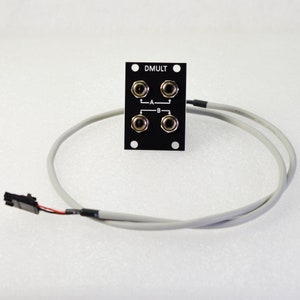 Pu&ograve; includere: Un componente elettronico nero con la scritta "DMULT", con quattro prese di ingresso e un cavo grigio. Il componente ha una forma rettangolare con fori di montaggio. Il cavo ha un connettore.