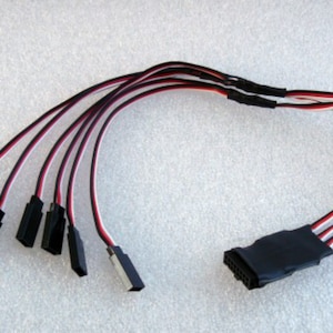 May include: A black and red wire splitter with six black connectors on one end and a black connector with multiple pins on the other end.