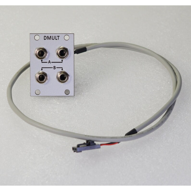 Pu&ograve; includere: Un modulo elettronico color argento con quattro prese di ingresso, etichettate A e B, e il testo "DMULT". Un cavo grigio con un connettore si estende dal modulo.