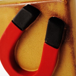 May include: A red and black horseshoe magnet attached to a brown ceramic surface.