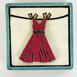 May include: A red dress with a black belt hangs on a clothesline with gold clothespins. The dress is on a white background with a blue border.